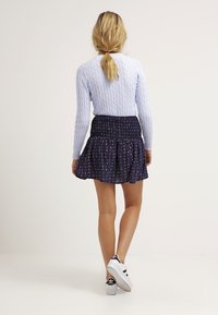 Blauwe kabeltrui gecombineerd met een marineblauwe rok met kleurrijke geometrische patronen, afgemaakt met witte sneakers.