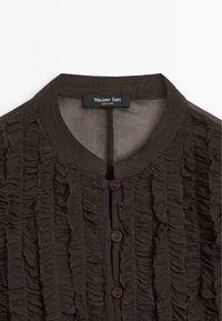Camicia texture marrone scuro con strisce verticali arricciate e scollatura tonda, abbottonata davanti con tre bottoni visibili.