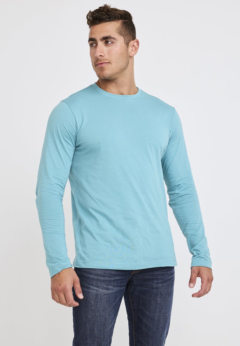 Lichtblauw shirt met lange mouwen, gemaakt van een zachte, lichte stof met een ronde hals, gecombineerd met donkere denim jeans.