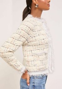 Texturēts krēmkrāsas kardigāns ar krāsainām diegam, ar franje apdari gar apkakli un piedurknēm, kā arī pieguļošu dizainu ar priekšējām kabatām.