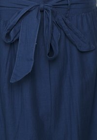 Vestido azul marino de tejido ligero, con detalle de cinturón atado, costuras visibles y un diseño fluido.