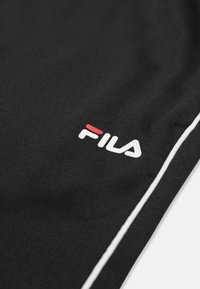 Tissu noir avec un petit logo FILA blanc et rouge, ainsi qu'un fin détail de rayure blanche le long du bord du vêtement.