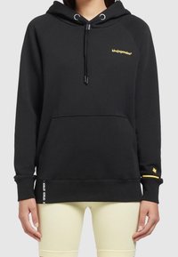 Czarna bluza z kapturem z kieszenią z przodu, regulowanym sznurkiem oraz żółtymi akcentami logo na klatce piersiowej i rękawie. Miękka tkanina z ściągaczami przy rękawach.