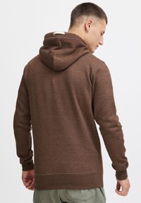 Sudadera con capucha marrón que presenta una tela texturizada, mangas largas y un cordón en la capucha. El dobladillo y los puños son acanalados.