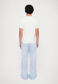 T-shirt branca de algodão com decote redondo, combinada com calças listradas em azul claro com pernas largas e uma textura subtil.