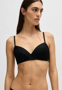 Reggiseno nero con design liscio e imbottito e dettagli testurizzati. Spalline sottili e scollatura a V. Accento minimalista con logo dorato.