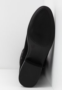 Suela de zapato de ante negro con una textura suave, que cuenta con una suela de goma texturizada para agarre y una forma elegante y redondeada.