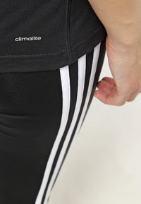 Leggings deportivos negros de material elástico con tres rayas verticales blancas a lo largo del costado y una etiqueta "climalite" en la cintura.