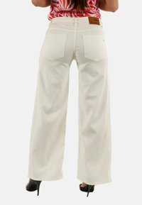 Jeans blancos de pierna ancha con una textura suave, que cuentan con dos bolsillos traseros y una etiqueta de cuero con la palabra "PLEASE" encima de la cintura.