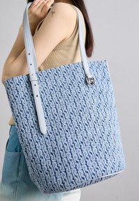 Blue textured tote bag with a woven pattern, featuring light blue leather straps and a silver hardware detail.