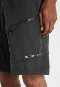 Schwarze Radsportshorts aus leichtem Stoff verfügen über eine Reißverschlusstasche und ein Logo "PROTEST CYCLING" an der unteren Seite.