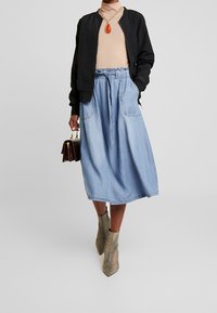 Svart bomberjacka, beige polotröja, ljusblå denimkjol med dragsko i midjan och beige hälstövlar med ormskinnsmönster. Brun handväska.