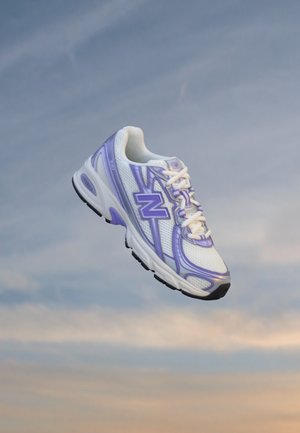 Chaussure de course New Balance blanche et violet clair flottant devant un ciel doux et nuageux.