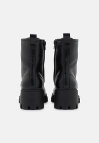 Bottes basses en cuir noir avec une semelle épaisse, des fermetures éclair latérales et des languettes au talon pour un enfilage facile. Texture lisse et design robuste.