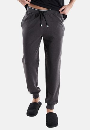 Charcoalgraue Sweatpants aus weichem Stoff mit einer lockeren Passform, elastischem Bund und Zugband. Kombiniert mit schwarzen Hausschuhen.