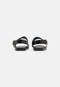 Svarta lackläder sandaler med platt sula, justerbar rem och detaljer i guldspänne. Har en slät yta och minimalistisk design.