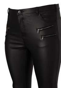 Svarta byxor i konstläder med framknapp, bälteshällor och fyra horisontella dragkedjefickor på låren.