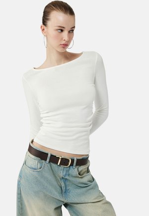 Hvid langærmet top med bådudskæring, der har en tætsiddende pasform og blød tekstur, parret med lyseblå baggy jeans og et brunt bælte.