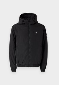 Czarna kurtka z kapturem, z przodu zamek błyskawiczny, elastyczne mankiety i dół, małe białe logo "cK" na lewej piersi oraz naszywka na lewym rękawie.