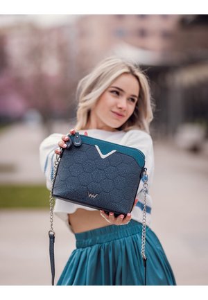Türaqua- und dunkelblaue strukturierte Handtasche mit einer rissigen Textur, silbernem Zubehör und einem Kettenriemen. Verfügt über ein dekoratives Logo auf der Vorderseite.