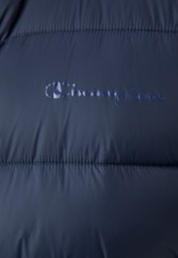 Marineblaue Steppjacke mit gequilteter Textur, featuring geprägtem "Champion"-Logo in passender Farbe. Glatter, strapazierfähiger Stoff.