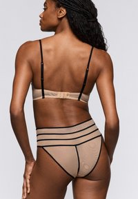 Naadloze beige mesh beha met verstelbare zwarte bandjes en haaksluiting, gecombineerd met hoog uitgesneden beige slips met zwarte horizontale strepen.