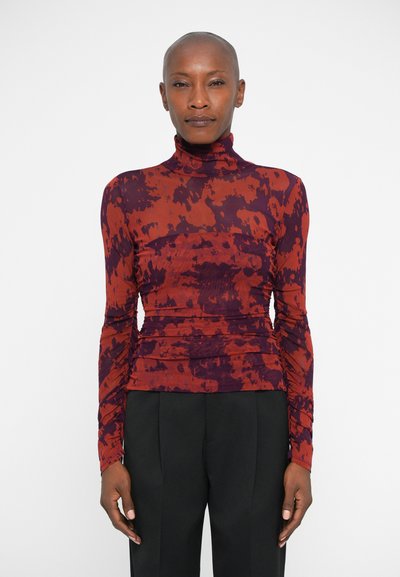 Haut à manches longues avec col roulé dans un motif abstrait rouge et violet. Présente des détails froncés sur les côtés, conçu en tissu léger.