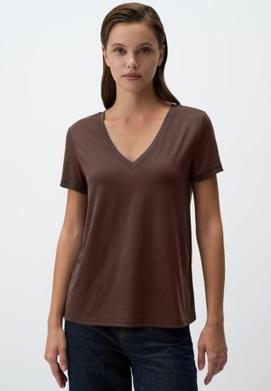 T-shirt marron à col en V en tissu doux, à manches courtes, coupe décontractée, associé à un jean sombre. Design minimal, sans motifs ni matériel visible.