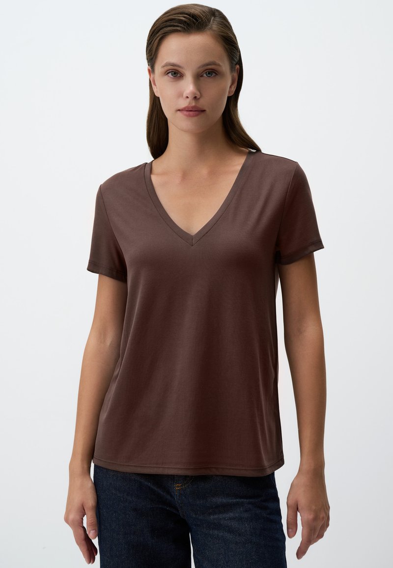 Maglietta a V marrone in tessuto morbido, con maniche corte, vestibilità rilassata, abbinata a jeans scuri. Design minimal, senza motivi né componenti visibili.