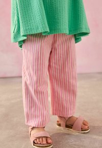 Top verde texturizado, pantalones anchos a rayas rosas y blancas, y sandalias ligeras rosas con suela plana y correa con hebilla.