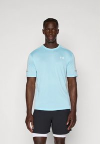 Hele sinine sportlik särk, valmistatud siledast ja hingavast kangast, lühikeste varrukatega ja ümmarguse kaelusega; kombineeritud mustade lühikestega.