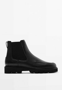 Botte Chelsea en cuir noir avec panneaux latéraux élastiques, languette au talon, et semelle crantée épaisse pour une meilleure traction.