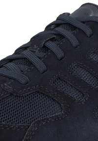 Navy blue athletic shoe featuring a mesh material, suede accents, and textured laces. Notable stitching detail and ventilation openings.