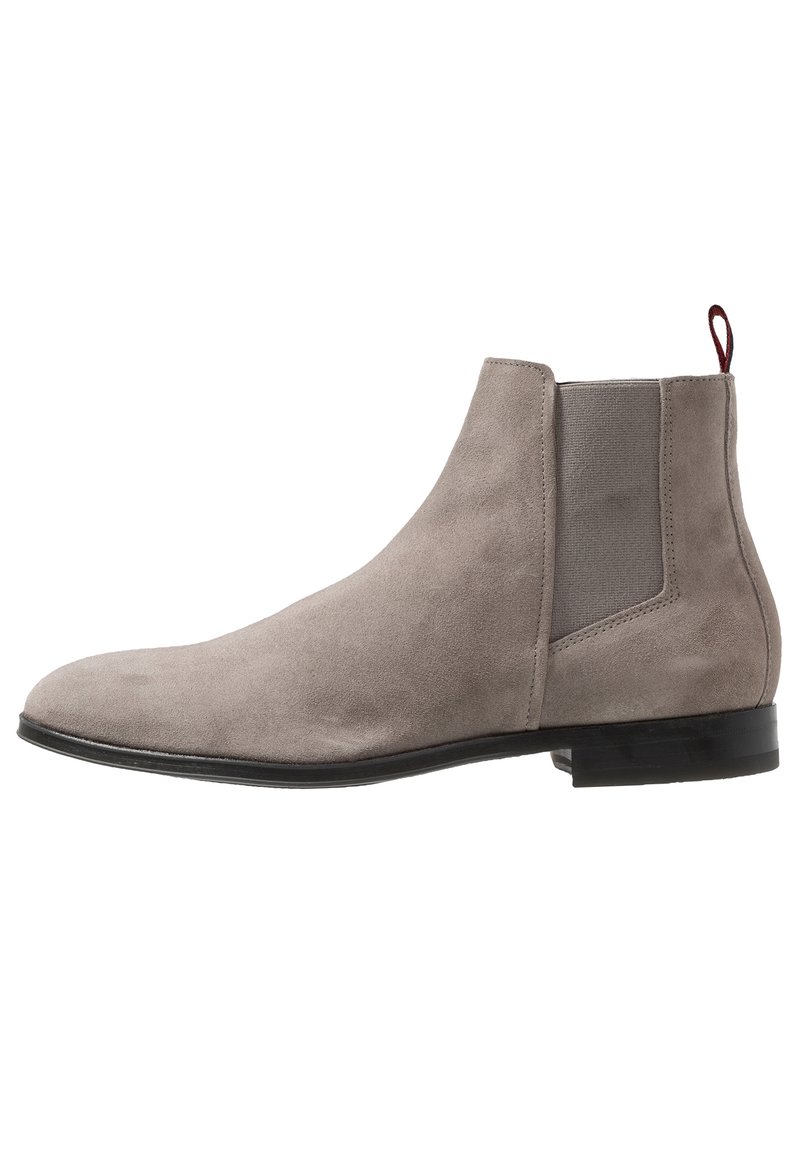 Bottines Chelsea en suède gris clair avec panneau latéral élastique, semelle noire et tirant rouge à l'arrière, présentées en profil latéral.