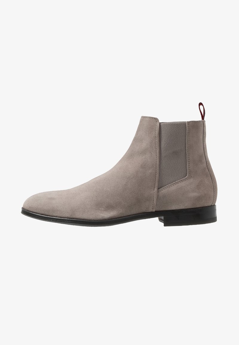 Bottines Chelsea en suède gris clair avec panneau latéral élastique, semelle noire et tirant rouge à l'arrière, présentées en profil latéral.
