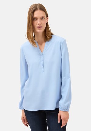 Blusa azzurra chiara con un leggero scollo a V, dettagli in bottoni e polsini elasticizzati. Realizzata in un materiale liscio con una vestibilità comoda.