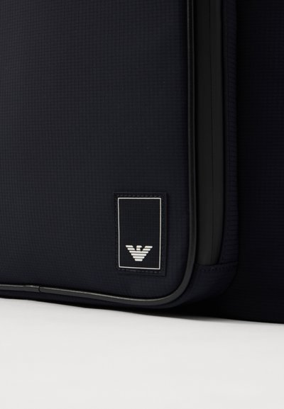 Τσαντάκι θαλάσσης σε ναυτικό μπλε, κατασκευασμένο από υφασμάτινη επιφάνεια με υφή, διαθέτει μαύρο φερμουάρ και άσπρη ετικέτα λογότυπου με γεωμετρικό σχέδιο.