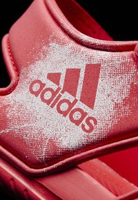 Sandalia deportiva roja con un upper texturizado. Presenta un gran logo blanco de "adidas" y un diseño de correas seguras. Material suave con un acabado liso.
