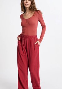 Czerwona bluzka z długim rękawem i zapinanym dekoltem, w połączeniu z luźnymi czerwonymi piżamowymi spodniami w kratkę z kieszeniami bocznymi i elastycznym pasem.