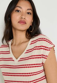 Top de punto con escote en V y mangas cortas, con una base beige y rayas horizontales rojas, de tejido texturizado y liviano.