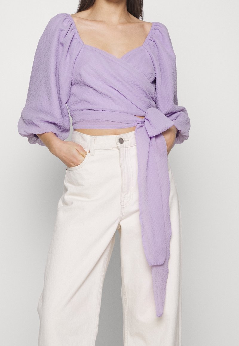 Lavendel omslagstopp med puffärmar, texturerad tyg, v-ringning och knytdetalj i midjan. Matchas med off-white högmidjade byxor.