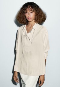 Lichtbeige oversized shirt met korte mouwen, een knoopsluiting, een enkele borstzak en een gestructureerde stof.