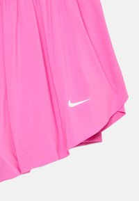 Różowa spódnica sportowa wykonana z lekkiego materiału. Posiada zaokrąglony dół oraz biały akcent logo Nike z boku. Gładka tekstura.