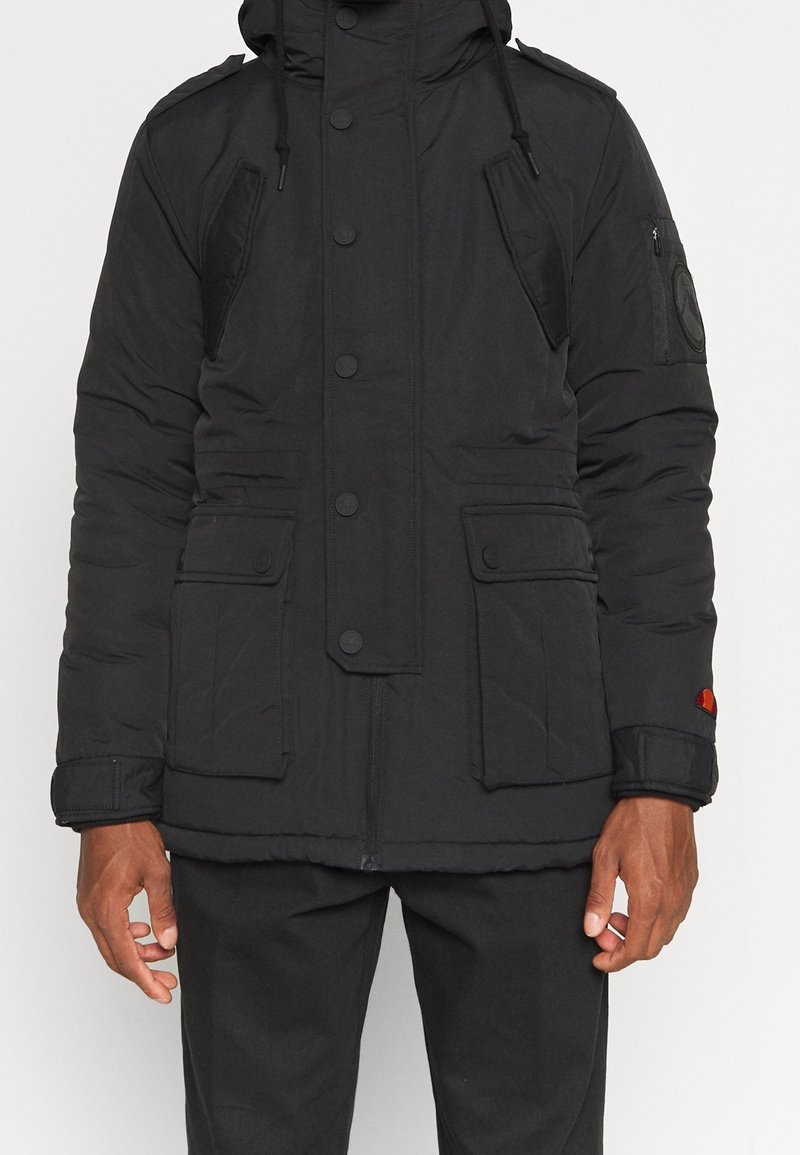 Veste rembourrée noire avec capuche, dotée de boutonnage, de multiples poches et d'un tissu texturé. Comprend des patchs décoratifs sur les manches.