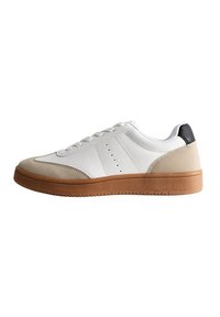 Vit lädersneaker med beige mockadetaljer, platt gummisula, rund tå och kontrasterande svart häldetalj. Har perforerad design.