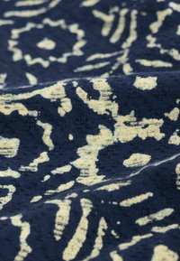 Námorně modrý textil s krémově zbarveným abstraktním vzorem s variabilními tvary a texturami, zahrnujícími tečky a víry, v tkanině.