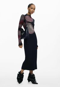 Must pikk kleit soonilise tekstuuriga, millel on värviline triibuline topp. Komplekti kuuluvad must käekott ja eriliselt volditud mustad pahkluukingad.