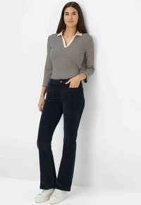 Navy ribcordbroeken met een lichte flare, aangevuld met een gestreept langemouwen top met een beige kraag. Casual witte sneakers.
