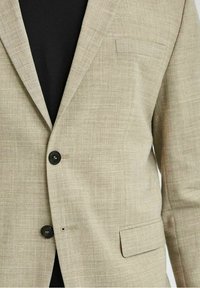 Beige linneblazer med en texturerad yta, enkel knappstängning och sydd axeldetalj. Har ett slitsat slag och sidficka.