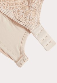 Lace and soft fabric bra in light beige, featuring intricate floral lace at the top and a hook and eye closure with multiple adjustment options.